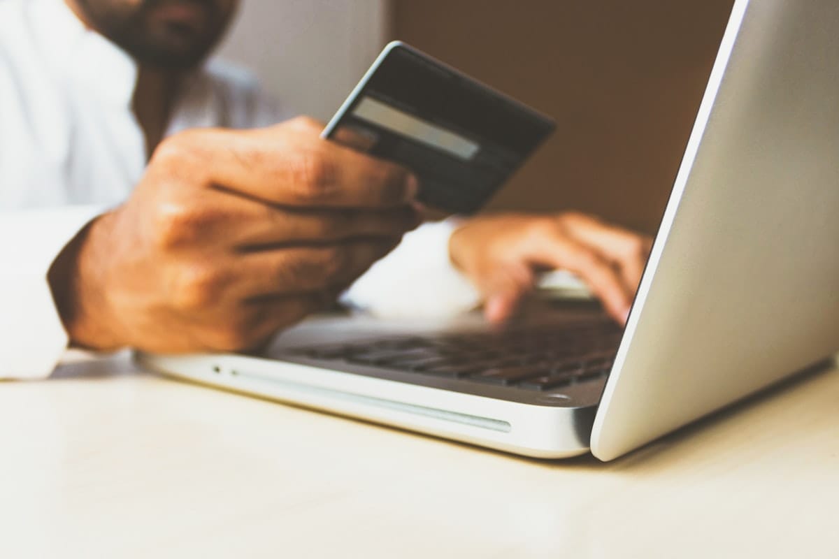 Osoba składająca zamówienie online za pomocą laptopa i karty płatniczej przy stole