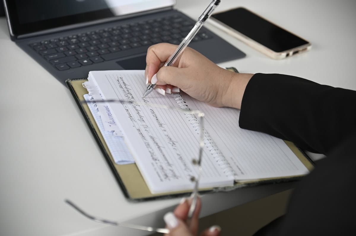 Osoba zapisuje notatki w zeszycie przy otwartym laptopie — planowanie treści na stronę internetową firmy